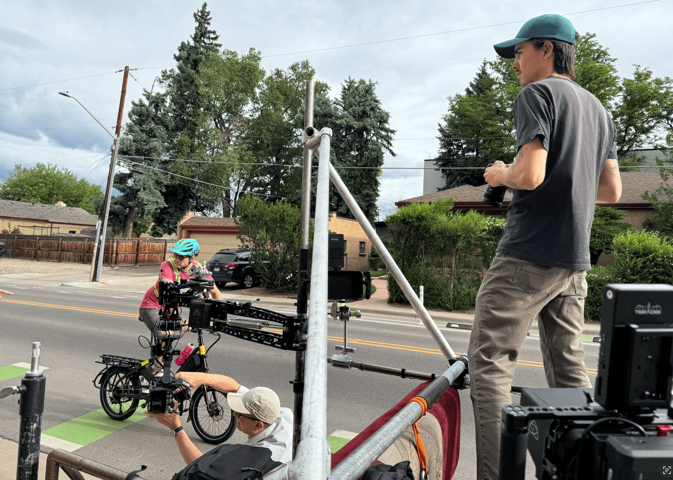 Behind-the-scenes setup of a film shoot featuring a cyclist on a cargo bike, with a mounted camera rig and crew members adjusting equipment on a street.